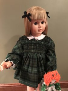 Blonde companion doll in a green plaid dress holding raggedy ann